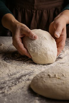 A baker's hands kneading fresh dough on a floured surface for bread making.