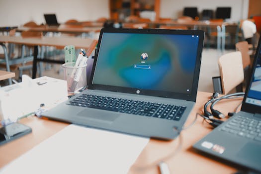 A close-up of a laptop on a desk in a classroom setting, ready for educational use.