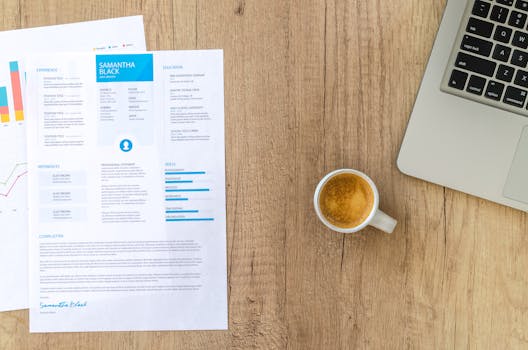 Top view of a desk with resume, coffee cup, and laptop on a wooden surface, ideal for business concepts.